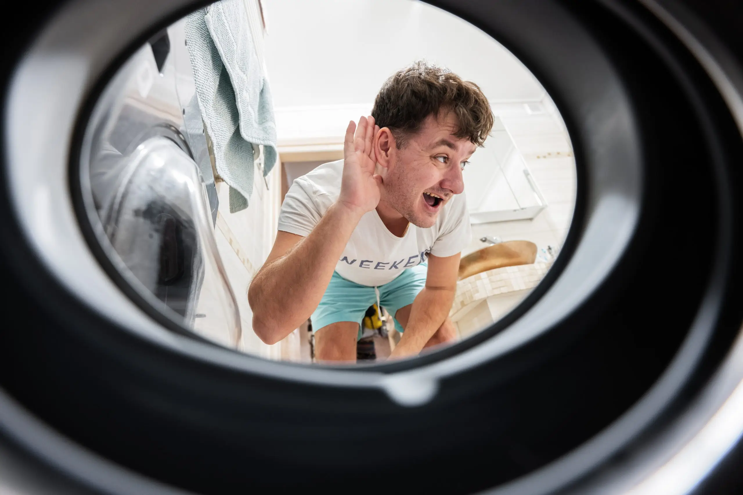 A man is listening to a washing machine for a squeaking sound.